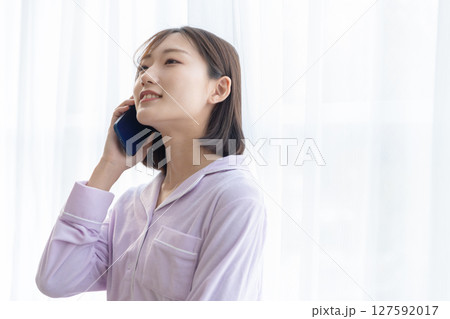 窓辺でパジャマを着て電話をしている若い女性 127592017