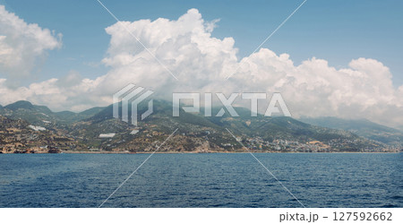 Scenic coastal landscape with blue sea, mountain ridge and dramatic clouds over a Mediterranean town. Summer travel, Clouds descend on the mountains. Panorama seascape with mountains and clouds Scenic coastal landscape with blue sea, mountain ridge and dramatic clouds over a Mediterranean town. Summer travel, Clouds descend on the mountains. Panorama seascape with mountains and clouds 127592662