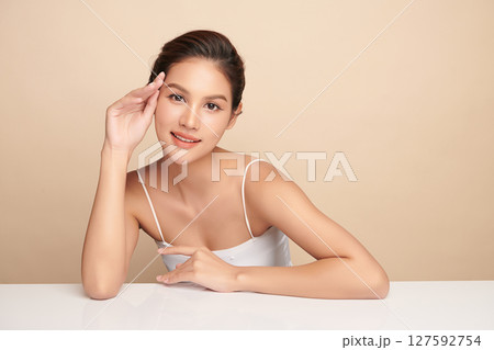 A beautiful young Asian woman with clean, fresh skin against a beige background. Skincare, facial treatment, cosmetology, beauty, and spa. An elegant portrait of an Asian woman. 127592754