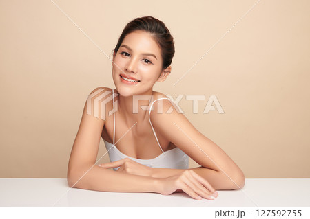 A beautiful young Asian woman with clean, fresh skin against a beige background. Skincare, facial treatment, cosmetology, beauty, and spa. An elegant portrait of an Asian woman. 127592755