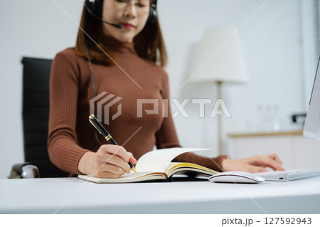 Friendly smiling female call-center agent with headset working on support hotline in office. Friendly smiling female call-center agent with headset working on support hotline in office. 127592943