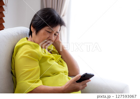 Senior asian woman stress and worried sitting on sofa while looking on smart phone in living room. 127593067