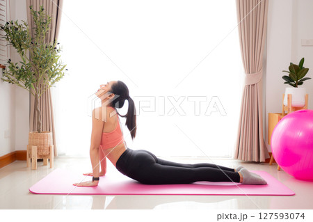 Young asian woman practicing Yoga with stretching muscle back on yoga mat in living room. Young asian woman practicing Yoga with stretching muscle back on yoga mat in living room. 127593074