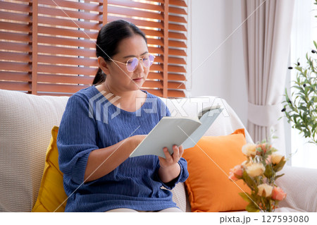 Asian senior woman reading a book sitting on sofa with relax in living room at home. Asian senior woman reading a book sitting on sofa with relax in living room at home. 127593080