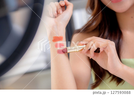 Closeup hands young asian beauty influencer testing multiple lipstick shades on arm. Closeup hands young asian beauty influencer testing multiple lipstick shades on arm. 127593088