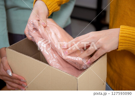 Closeup hand of woman packing in cardboard box for shipping or storage in home office. Closeup hand of woman packing in cardboard box for shipping or storage in home office. 127593090