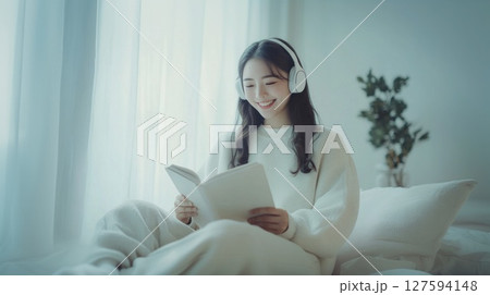 Person wear headphone sit on sofa and read book. 127594148