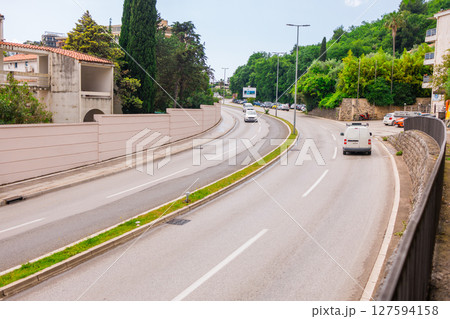 City street with cars and Mediterranean greenery in Montenegro. Urban infrastructure and road transportation in a coastal town. 127594158