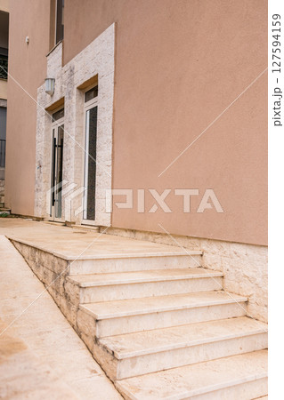 Modern residential entrance with marble stairs and beige wall. Urban architecture and Mediterranean building design in Montenegro. Modern residential entrance with marble stairs and beige wall. Urban architecture and Mediterranean building design in Montenegro. 127594159