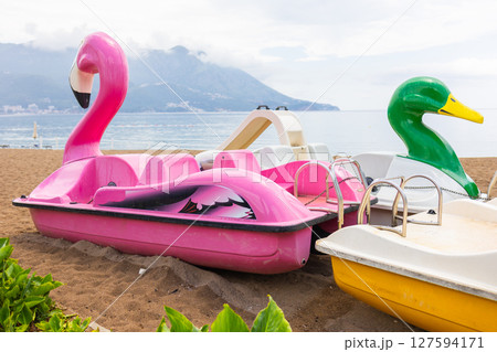 Colorful flamingo and duck paddle boats on the beach before summer rides. Playful seaside leisure, family vacation and coastal amusement atmosphere. 127594171