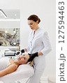 Mature woman receiving anti-aging skin treatment lying in cosmetic clinic. Cosmetologist performing photorejuvenation face procedure using professional aesthetic laser machine, skincare and wellness 127594463
