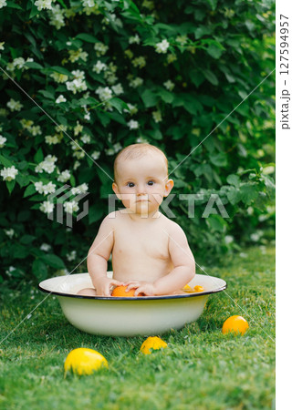 Baby Playing in Tub Surrounded by Oranges Outdoors Baby Playing in Tub Surrounded by Oranges Outdoors 127594957