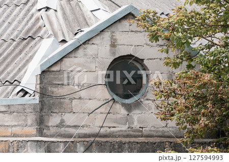 Round Window on Gray Stone Wall, Roof Detail, Architectural Feature, Exterior View, Branch, Tree, Sunlight, Texture, Rustic Style, Urban Scene. 127594993