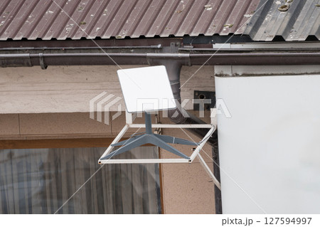 Satellite Dish Mounted on Building Exterior, Gray Metal Structure with Concrete Wall, Residential Scene, Outdoor Communication Technology 127594997