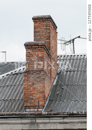 Aged Brick Chimney on Corrugated Iron Roof, Outdoor View, Rusty Tones, Architectural Detail, Grey Sky, TV Antenna, Vintage Style. Aged Brick Chimney on Corrugated Iron Roof, Outdoor View, Rusty Tones, Architectural Detail, Grey Sky, TV Antenna, Vintage Style. 127595008