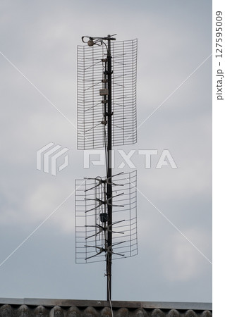 Rooftop Television Antenna Stack Against Cloudy Sky, Vintage Aerial Communications Tower, Outdoor Signal Reception, Gray Metal Structure. 127595009