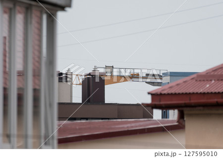 Construction Crane Over Rooftops: Gray Sky, Industrial Landscape, Urban Development, Building Structures, Modern Architecture View. 127595010