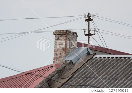 Old Brick Chimney on a Slanted Red Tile Roof with Power Lines Against a Cloudy Sky, Rustic Urban Architecture 127595011