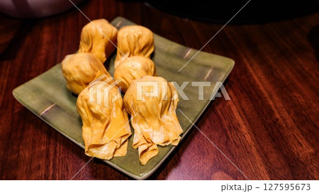 close up of six pieces of uncooked raw shrimp and pork stuffed dumplings on a plate on a wooden table with copy space 127595673