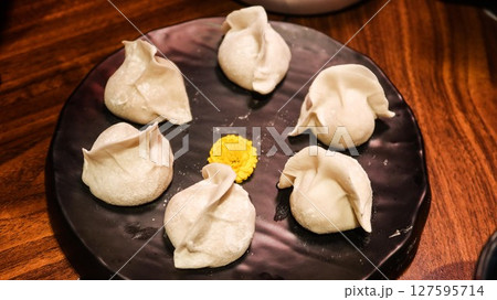 close up of six uncooked raw pork dumplings (Jiaozi or Gyoza) on a plate with a yellow flower in the middle for decoration 127595714