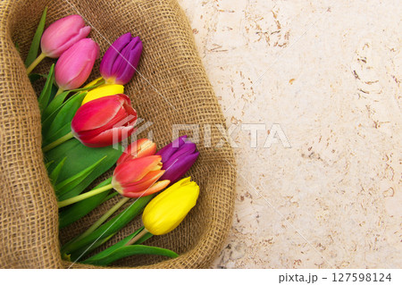 Multicolor tulips bouquet in natural fabric wrapping paper. Spring flowers on the cork background . Top view with place for text. Copy space. 127598124