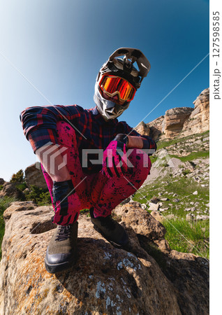 Close-up portrait of young sportsman wearing protective helmet and protective mask on his face. Mature guy resting looking at camera after hard training in mountains Close-up portrait of young sportsman wearing protective helmet and protective mask on his face. Mature guy resting looking at camera after hard training in mountains 127598585