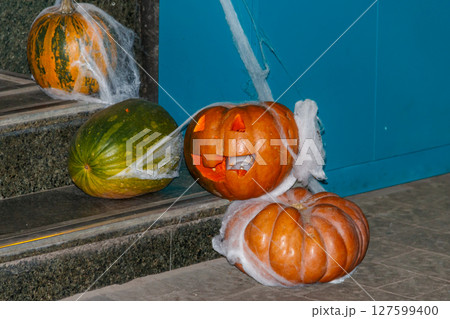 Spooky Halloween pumpkin jack-o-lanterns with spider web on the steps at a door. Decorations for Halloween holiday Spooky Halloween pumpkin jack-o-lanterns with spider web on the steps at a door. Decorations for Halloween holiday 127599400