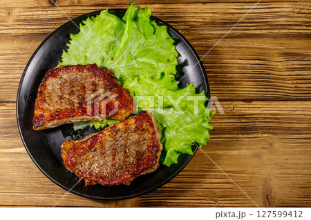 Grilled pork steaks with lettuce leaves on wooden table. Top view 127599412