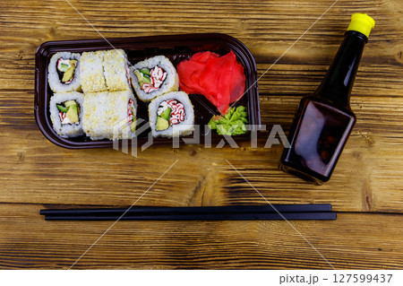Uramaki sushi rolls with surimi in plastic box on wooden table. Top view. Sushi for take away or delivery of sushi in plastic container Uramaki sushi rolls with surimi in plastic box on wooden table. Top view. Sushi for take away or delivery of sushi in plastic container 127599437