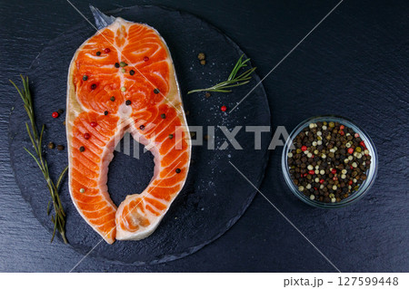 Raw salmon steak with spices on black slate. Top view 127599448