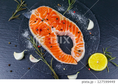 Raw salmon steak with spices on black slate. Top view 127599449