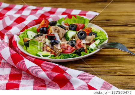 Tasty tuna salad with lettuce, black olives and fresh vegetables on wooden table 127599473