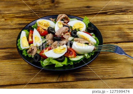 Tasty tuna salad with lettuce, black olives, eggs and fresh vegetables on wooden table 127599474