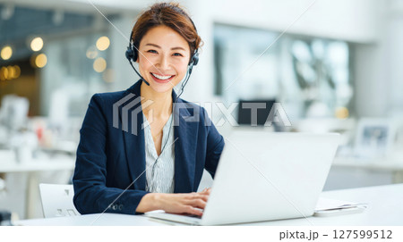 ヘッドセットを着けて笑顔で顧客対応するコールセンターの女性 127599512