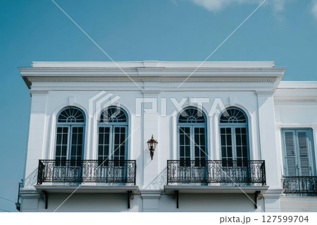 Sleek White Building Facade Rising Below Blue Sky with Elegant Arches and Balconies Sleek White Building Facade Rising Below Blue Sky with Elegant Arches and Balconies 127599704