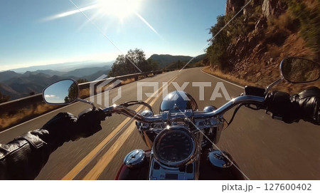 A motorcyclist rides a Harley-Davidson along a winding mountain road under the bright afternoon sun 127600402