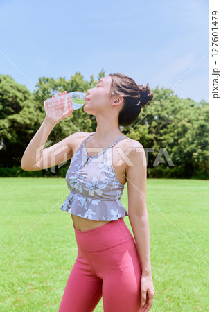 青空の天然芝でヨガ後に水分補給をする健康的な女性 127601479