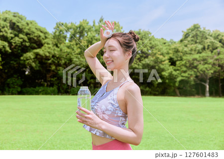 青空の天然芝でヨガ後に水分補給をする健康的な女性 青空の天然芝でヨガ後に水分補給をする健康的な女性 127601483