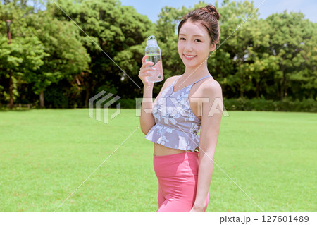 青空の天然芝でヨガ後に水分補給をする健康的な女性 127601489