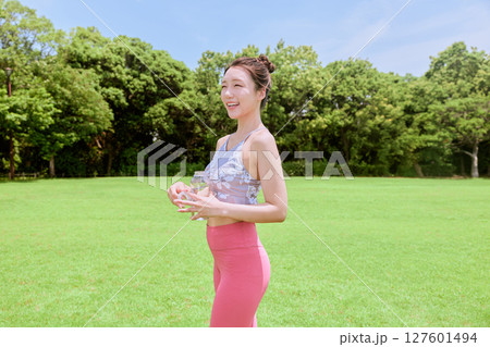 青空の天然芝でヨガ後に水分補給をする健康的な女性 127601494