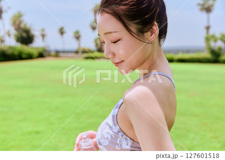 青空の天然芝でヨガ後に水分補給をする健康的な女性 青空の天然芝でヨガ後に水分補給をする健康的な女性 127601518