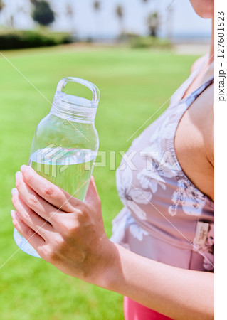 青空の天然芝でヨガ後に水分補給をする健康的な女性 青空の天然芝でヨガ後に水分補給をする健康的な女性 127601523