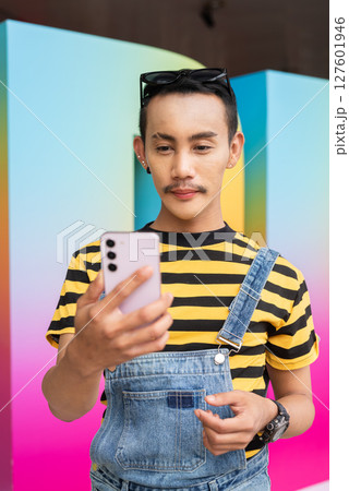 Empowering portrait of nonbinary genderfluid young Asian gay man using phone 127601946