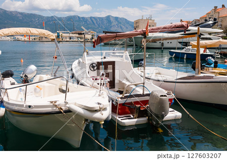 Motorboat moored in scenic marina with mountain background. Coastal lifestyle, nautical leisure, and summer tourism on waterfront. Motorboat moored in scenic marina with mountain background. Coastal lifestyle, nautical leisure, and summer tourism on waterfront. 127603207