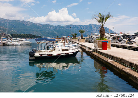 Motorboat moored in scenic marina with mountain background. Coastal lifestyle, nautical leisure, and summer tourism on waterfront. 127603224