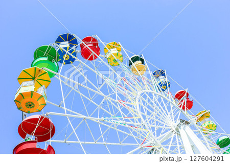 Colorful ferris wheel against a clear blue sky, showcasing vibrant gondolas and structure 127604291