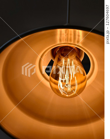 Close up of a glowing vintage light bulb in a warm colored lamp shade. 127604697