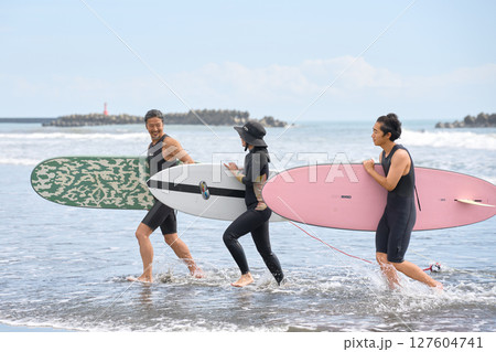 サーフィンを終えて笑顔で浜に戻る男女3人 127604741