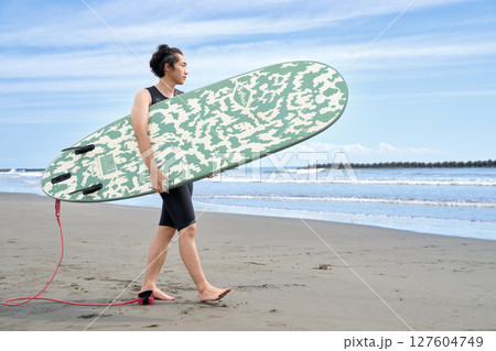 サーフボードを抱えて海辺を歩く若い男性 127604749