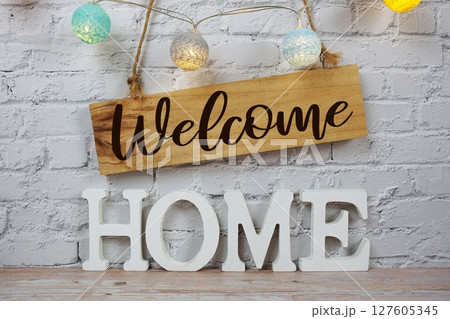 Welcome Home alphabet letters and wooden signboard hanging on white brick wall background Welcome Home alphabet letters and wooden signboard hanging on white brick wall background 127605345